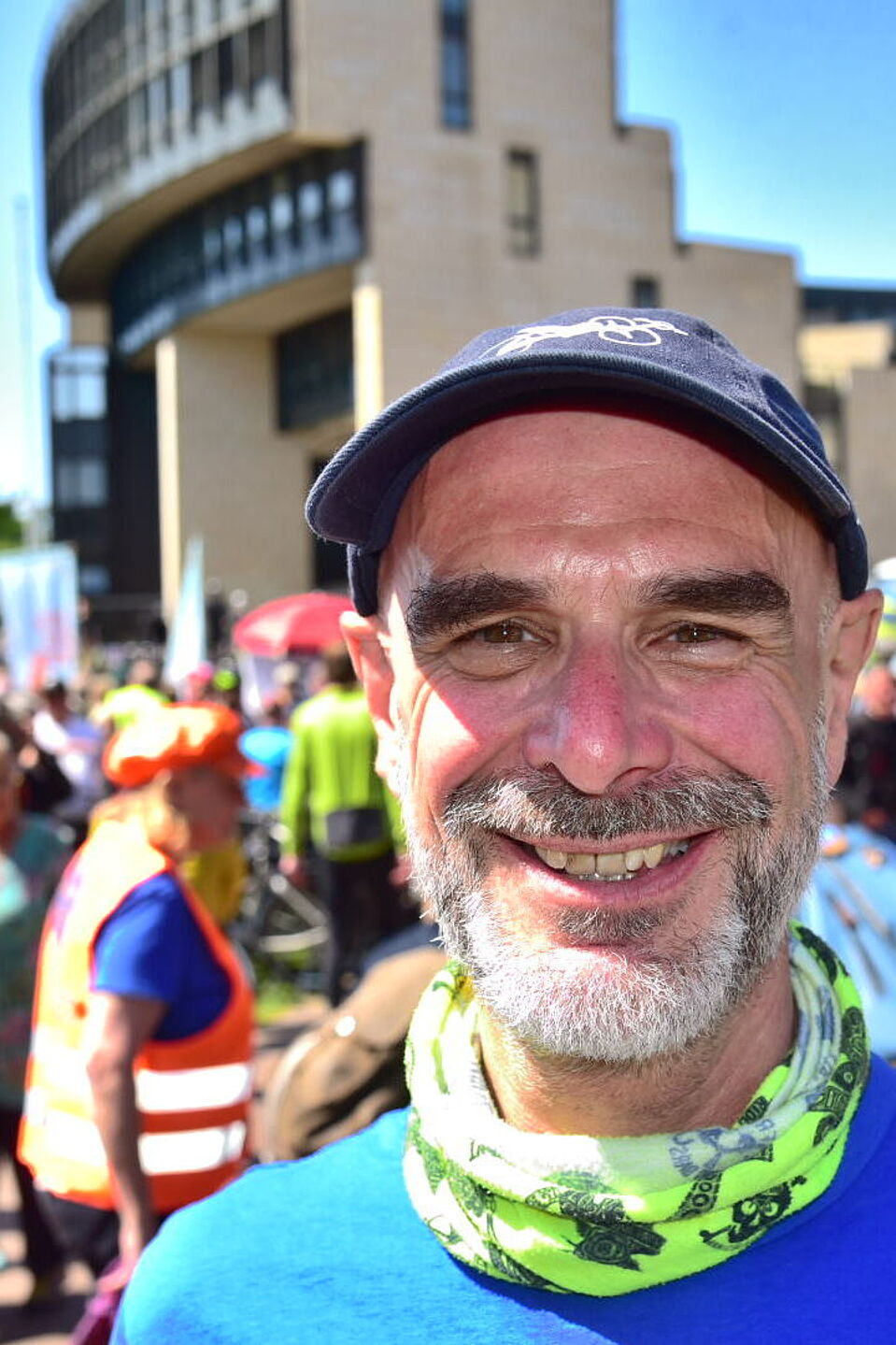 Axel Fell, Landesvorsitzender ADFC NRW Axel Fell, Landesvorsitzender des ADFC NRW, mit blauem T-Shirt und Mütze bei einer Fahrraddemo mit anderen Radfahrenden im Hintergrund vor dem NRW-Landtag in Düsseldorf.